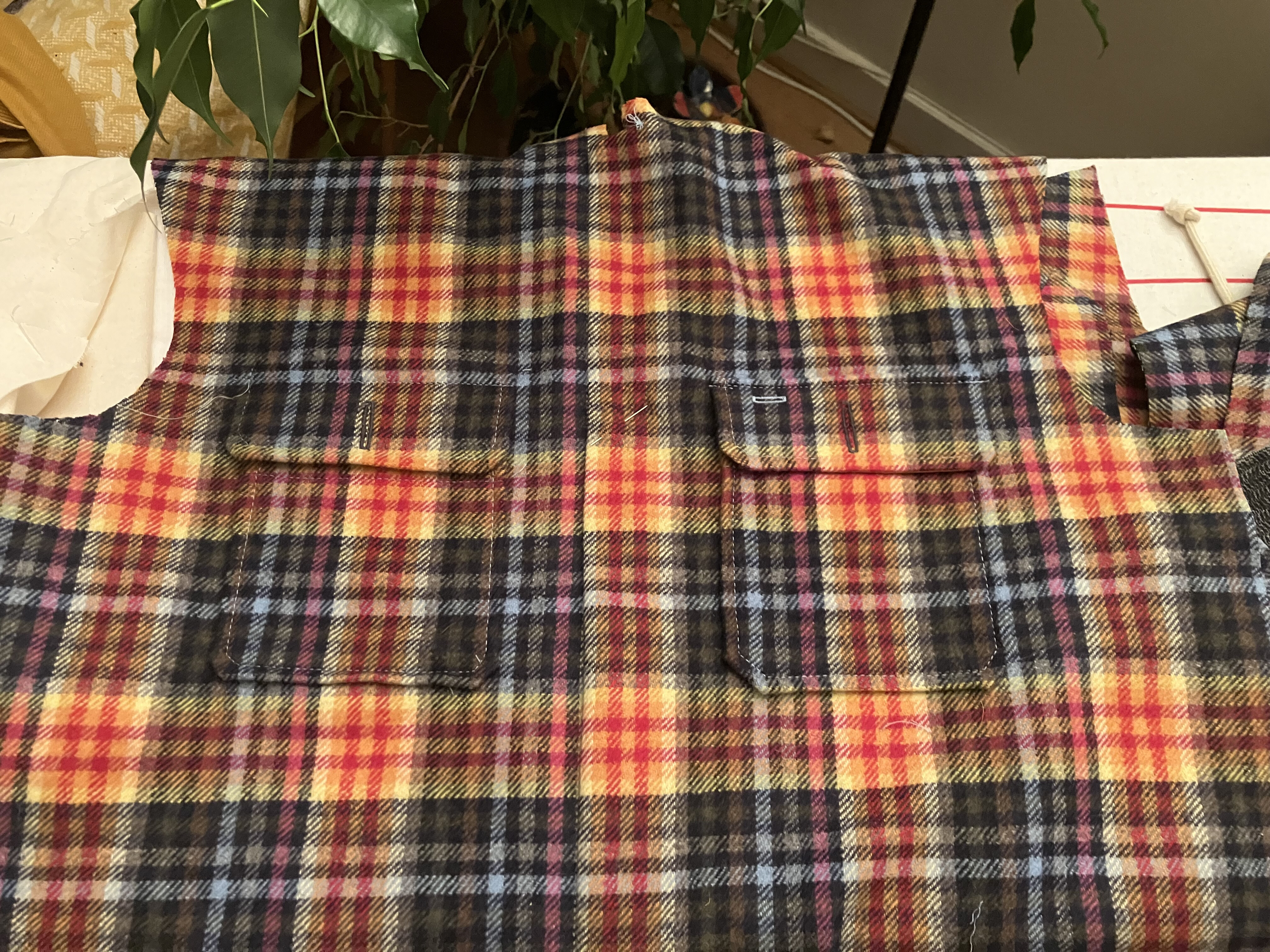 photo de construction de la surchemise, on voit les pièces de tissu en tartan à carreaux, je plaque des poches de poitrine qui ont le même motif ; la difficulté c’est de superposer les lignes pour ne pas avoir de décalage à la fin