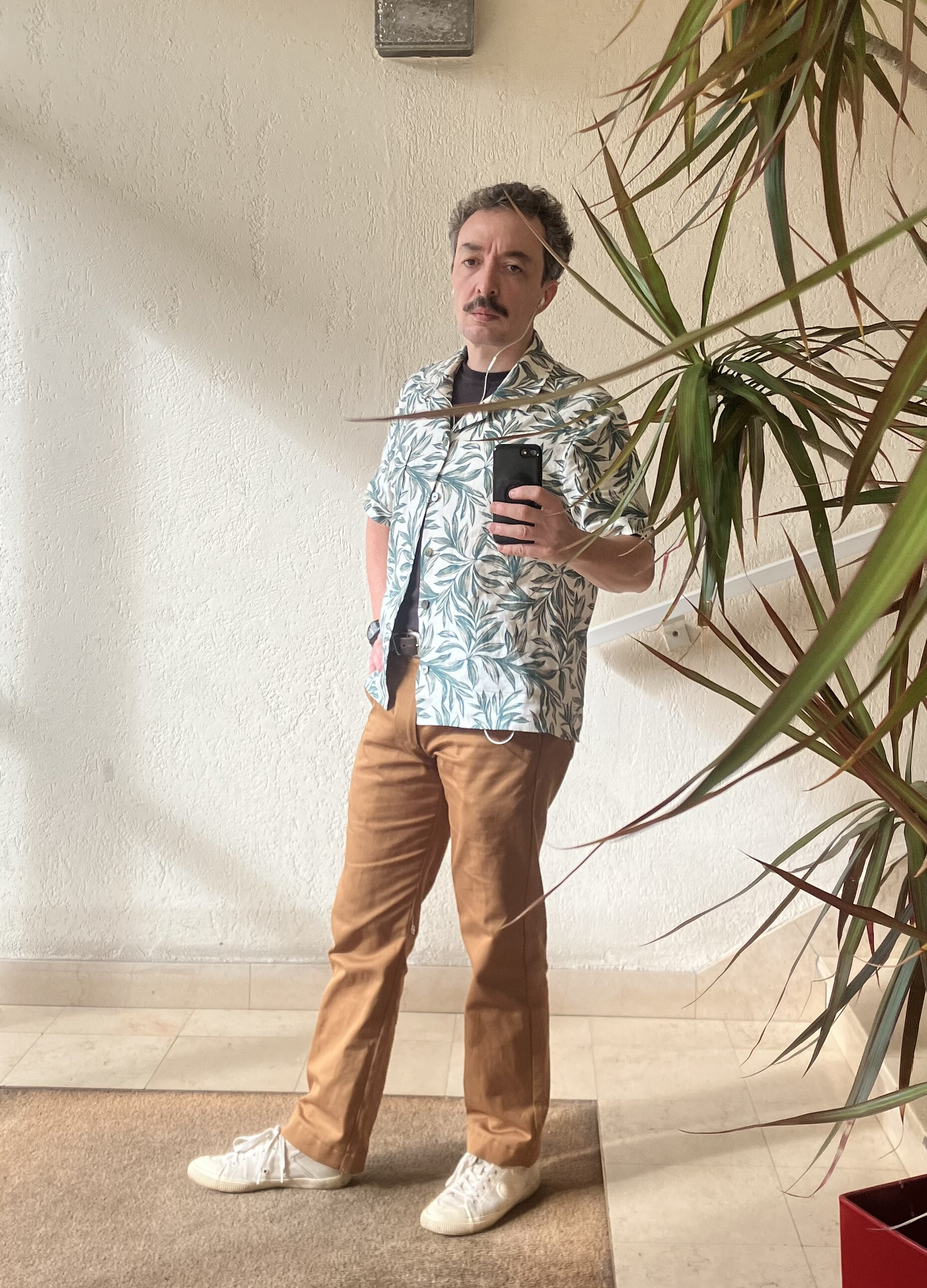 photo du même sujet, qui est habillé différemment : il porte une chemisette en lin clair à motif de feuilles, et un pantalon de type chino couleur terre